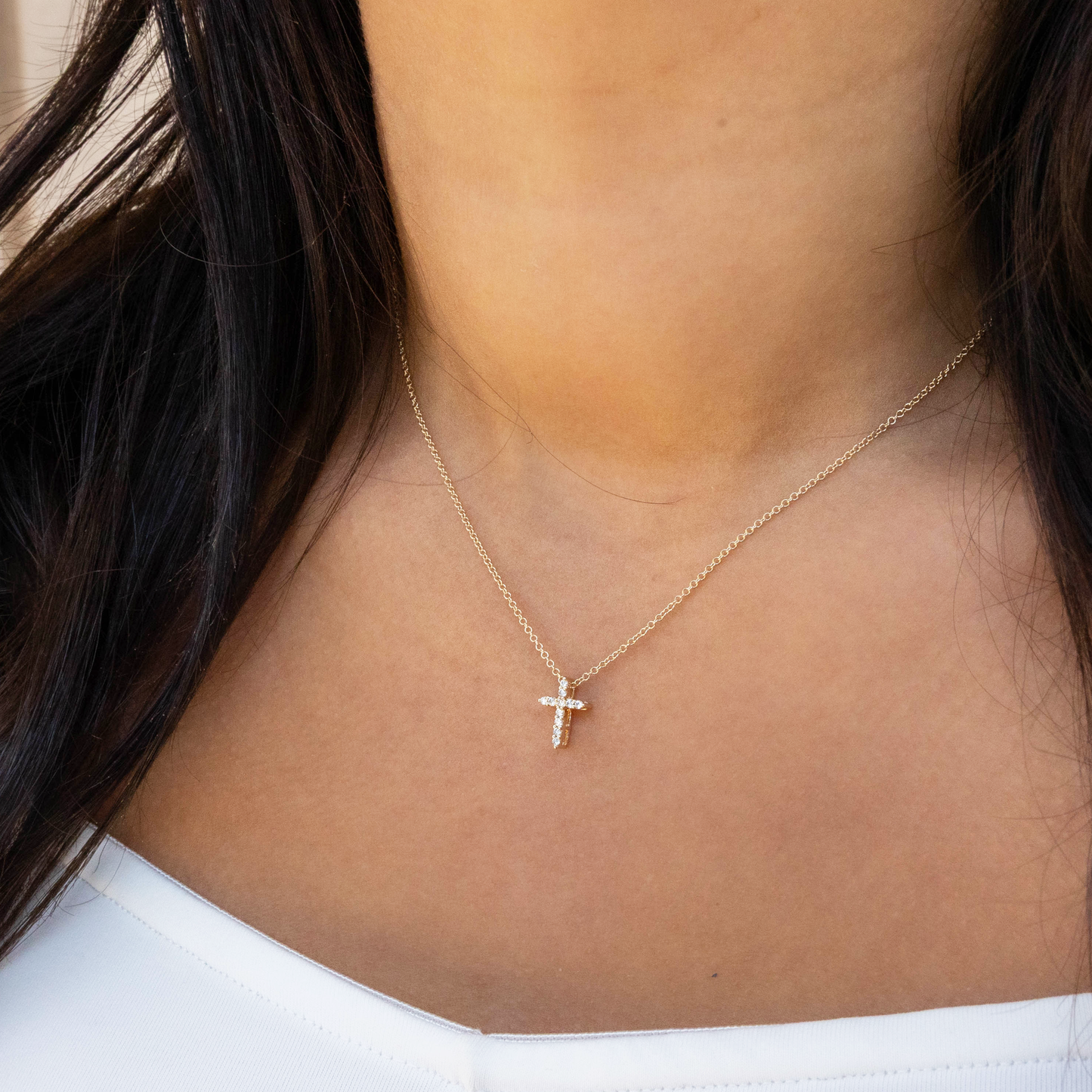 Gold necklace with a cross pendant on a person wearing a white top.