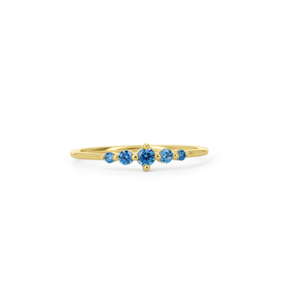 A delicate yellow gold ring featuring a row of five round-cut blue gemstones, set against a plain white background.