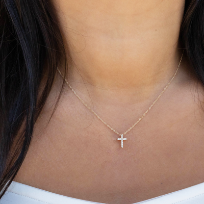 Rose gold necklace with a diamond cross pendant on a person's neck.