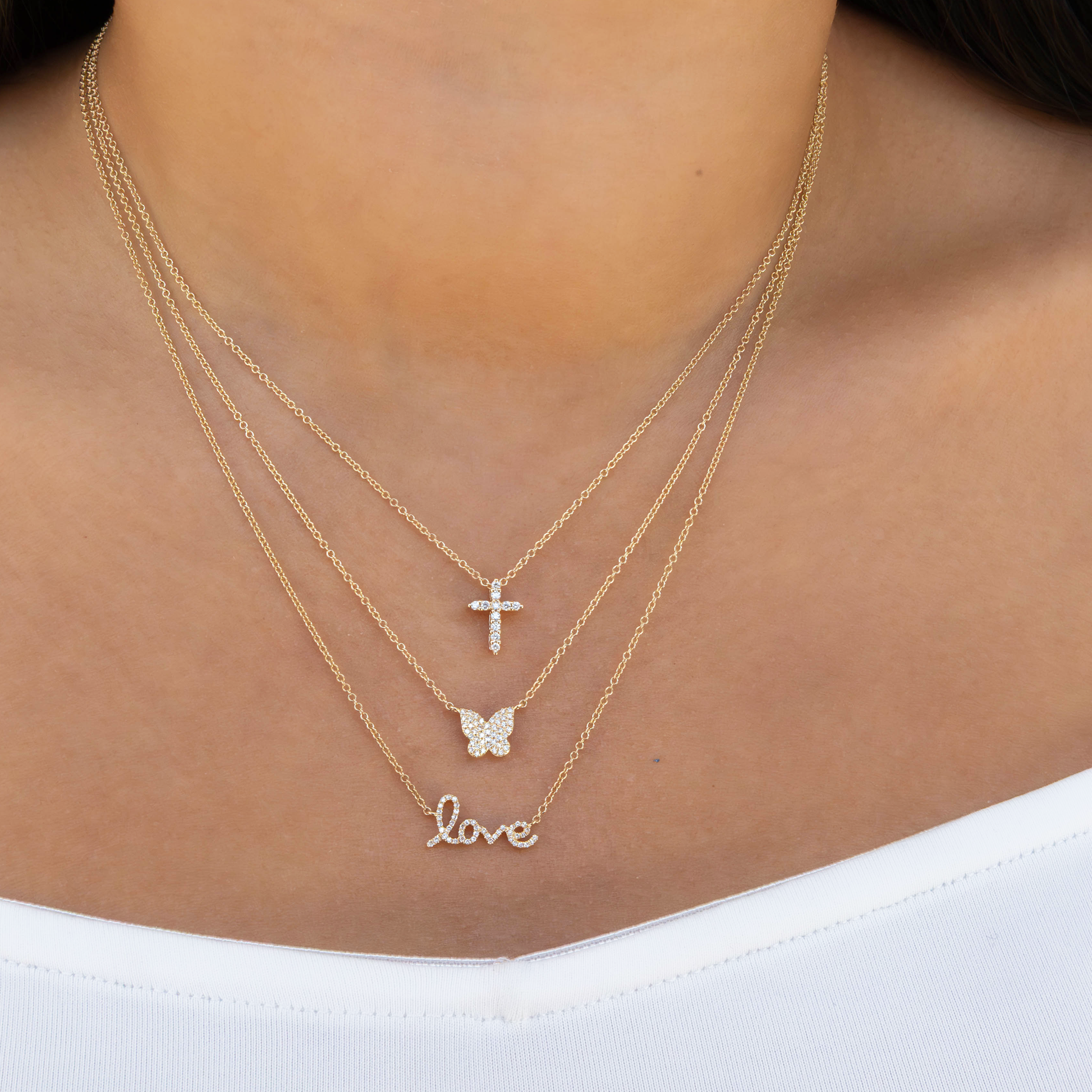 Diamond Cross layered with a diamond butterfly and diamond love script necklace in 14kt yellow gold. 