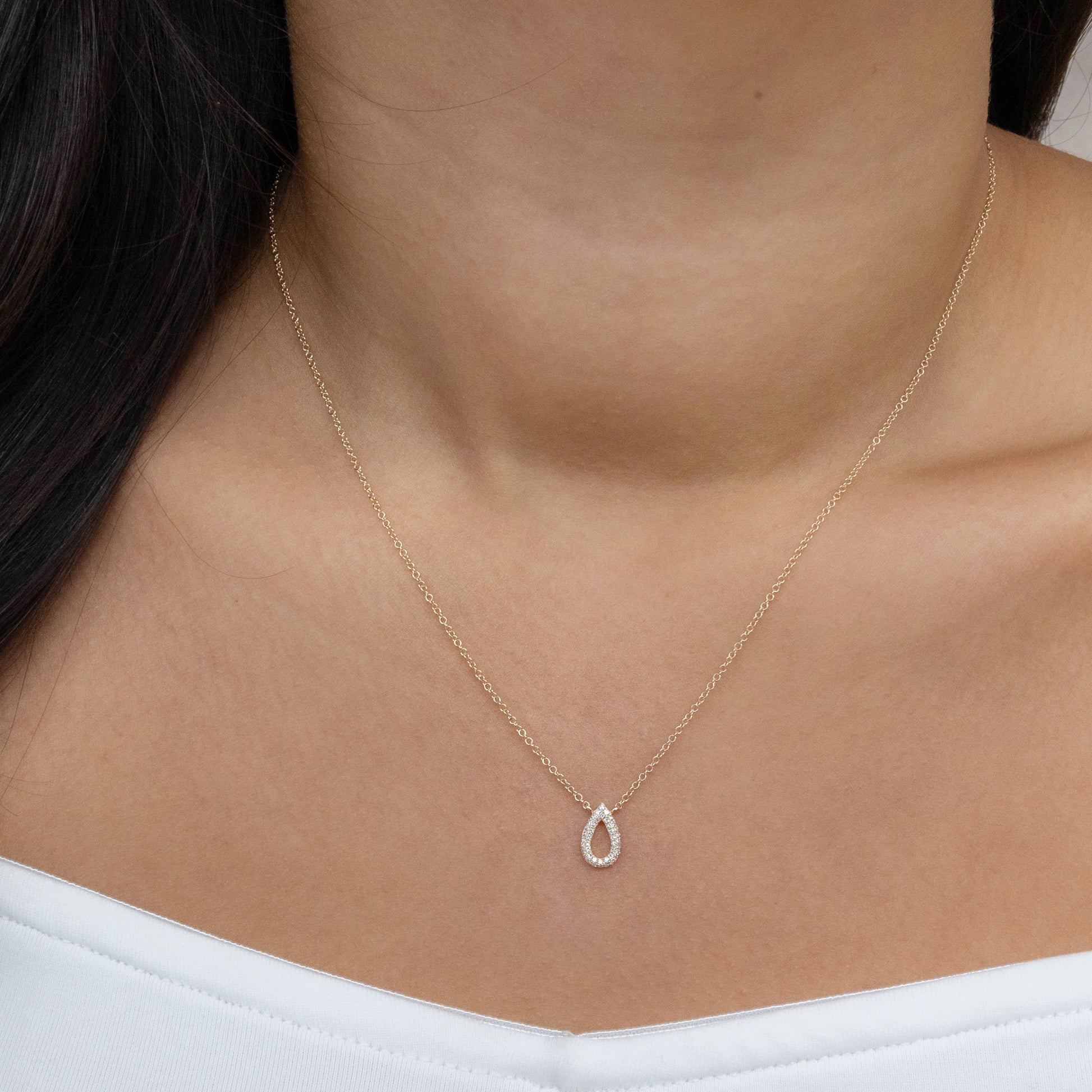 Gold necklace with a teardrop pendant on a person wearing a white top.
