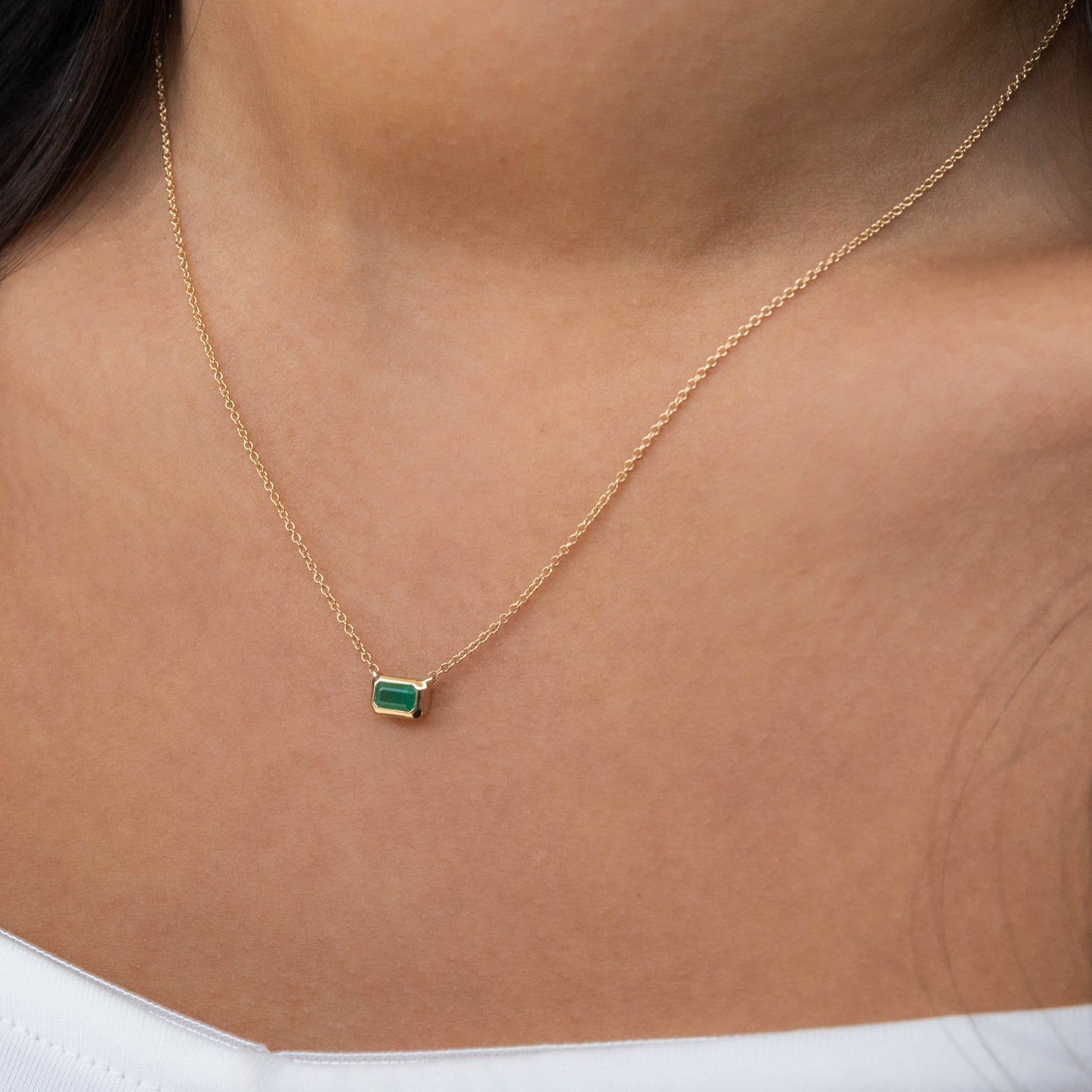 Gold necklace with a green gemstone pendant on a person's neck